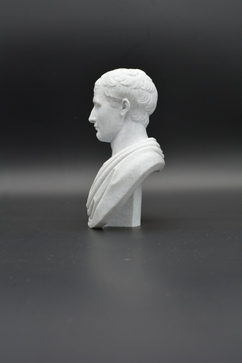 Puede incluir: Un busto de yeso blanco de un hombre con el pelo corto. El busto est&aacute; sobre un fondo negro liso.