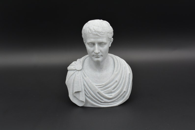 Puede incluir: Un busto de yeso blanco de un hombre con el pelo corto y una toga. El busto est&aacute; sobre un fondo negro.
