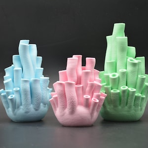 Peut inclure: Trois sculptures en céramique de corail de différentes couleurs : bleu clair, rose et vert. Chaque sculpture est composée de plusieurs tubes regroupés pour former une forme de corail.