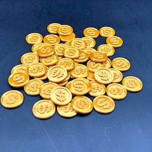 Puede incluir: Un conjunto de monedas de color dorado, cada una con un símbolo de dólar, dispersas sobre una superficie azul oscuro. Las monedas son redondas y parecen estar hechas de un material metálico, posiblemente plástico o metal.