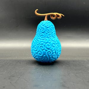 Puede incluir: Una fruta impresa en 3D azul y marrón con un patrón de espiral. La fruta tiene un tallo con una hoja.