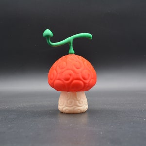 Könnte beinhalten: Eine rote und weiße Pilzfigur mit einem grünen Stiel. Der Pilz hat eine strukturierte Oberfläche und ein kleines grünes Blatt oben.