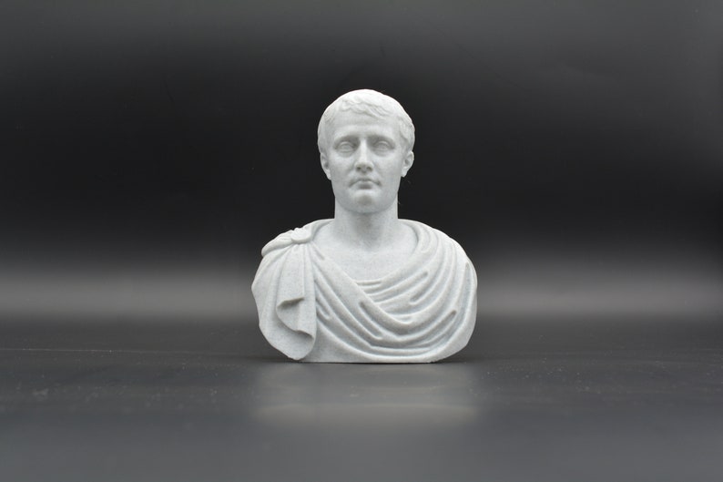 Puede incluir: Un busto de yeso blanco de un hombre con el pelo corto y una toga. El busto est&aacute; sobre un fondo negro.
