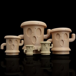 May include: A family of four beige ceramic sculptures with rounded shapes, oval cutouts, and small arm-like protrusions. The sculptures vary in size, with the largest being the tallest. The background is black.