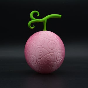 Peut inclure: Modèle 3D imprimé en rose et vert du "Fruit du Gomu-Gomu" de la série d'anime One Piece. Le fruit est une sphère avec un motif en spirale et une tige verte.