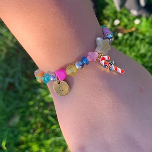 May include: A colourful beaded bracelet with a charm of a candy cane, a star, and a letter 'C'.
