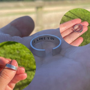 May include: Two silver rings with engraved messages. One ring says "I love you" and the other ring says "R&M" with a heart symbol.