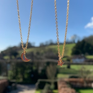 May include: Two gold necklaces with delicate chains. One necklace features a crescent moon pendant, while the other has a star pendant.