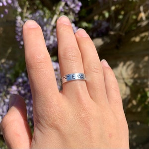May include: A silver ring featuring a single letter "E" and small flower designs around it.