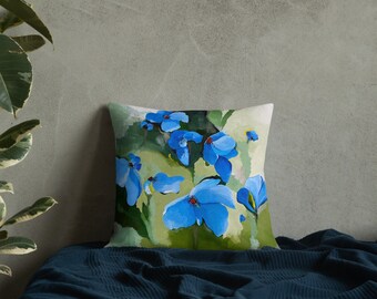 May include: A throw pillow featuring a blue floral design. The pillow has a watercolour-style painting of blue flowers with green leaves on a white background.
