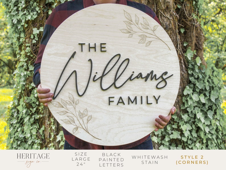 May include: A 24 inch round wooden sign with the text "THE Williams FAMILY" in black painted letters. The sign has a whitewash stain and a delicate floral design.