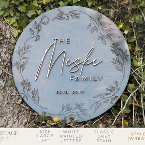 May include: A light blue round wooden sign with a floral wreath design. The sign says "The Meske Family Est. 2014".