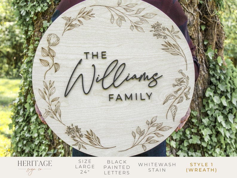 May include: A 24-inch round wooden sign with a floral wreath design. The sign says "The Williams Family" in black painted letters.