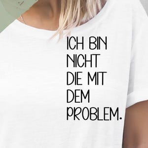 Könnte beinhalten: Weißes T-Shirt mit dem Aufdruck "Ich bin nicht die mit dem Problem." auf der Vorderseite. Der Text ist in Schwarz. Das Shirt ist in verschiedenen Größen und Farben erhältlich.