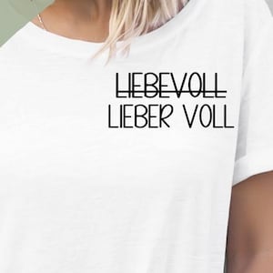 Könnte beinhalten: Weißes T-Shirt mit dem Aufdruck "LIEBEVOLL LIEBER VOLL" auf der Vorderseite. Der Text ist in Schwarz und hat eine moderne Schriftart. Das Shirt ist in verschiedenen Größen und Farben erhältlich.