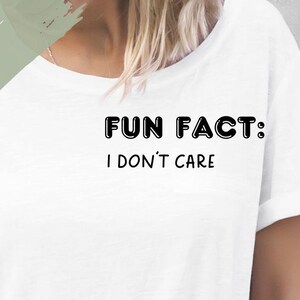 Könnte beinhalten: Weißes T-Shirt mit einem schwarzen Bügelbild, auf dem "Fun Fact: I don't care" steht. Der Text ist in fetter, umrahmter Schrift. Das Bild enthält auch den Text "Bügelbild" und "Verschiedene: - Größen - Farben".