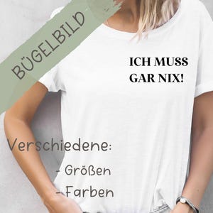 Könnte beinhalten: Weißes T-Shirt mit dem Aufdruck "ICH MUSS GAR NIX!" auf der Vorderseite. Der Text ist in Schwarz. Das Shirt ist in verschiedenen Größen und Farben erhältlich. Das Bild enthält auch den Text "Bügelbild" und "Verschiedene: - Größen - Farben".