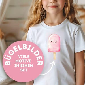 Könnte beinhalten: Weißes T-Shirt mit einer rosa Eis am Stiel-Grafik mit einem lächelnden Gesicht auf einem Holzstab. Ein rosa Kreis mit weißem Text, der "BÜGELBILDER, VIELE MOTIVE IN EINEM SET" lautet, befindet sich auf der linken Seite des Shirts.