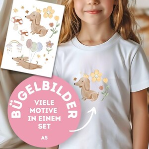 Könnte beinhalten: Weißes T-Shirt mit einem Aquarell-Dackel mit Krone, umgeben von gelben Blumen und Sternen. Ein Bogen mit passenden Bügelbildern mit verschiedenen Dackelmotiven, Pilzen und Luftballons ist ebenfalls zu sehen.
