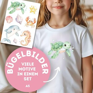 Könnte beinhalten: Ein weißes T-Shirt mit einem grünen Meeresschildkröten-Motiv. Ein Bogen Bügelbilder mit Meerestieren wie Schildkröte, Seestern, Krabbe, Delfin, Seepferdchen und Muscheln wird daneben gehalten. Auf dem Bogen steht der Text "BÜGELBILDER" und "VIELE MOTIVE IN EINEM SET".