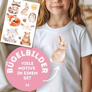 Könnte beinhalten: Weißes T-Shirt mit einer Aquarellillustration eines braunen Hasen mit Blumenkranz. Ein Bügelbildbogen mit Waldtiermotiven ist sichtbar. Der Bogen enthält einen Waschbären, einen Fuchs, einen Wolf, einen Bären und andere Kreaturen.