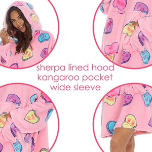 May include: Pink fleece blanket with a sherpa lining and a large kangaroo pocket. The blanket has a candy heart print with phrases like "Sleepin' Beauty" and "5 More Minutes".