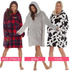 May include: Three oversized hooded blankets with different patterns. The first blanket is red and black plaid with the name "Camilla" embroidered on the front. The second blanket is grey with the name "Daisy" embroidered on the front. The third blanket is white with black cow print and the name "Emily" embroidered on the front.