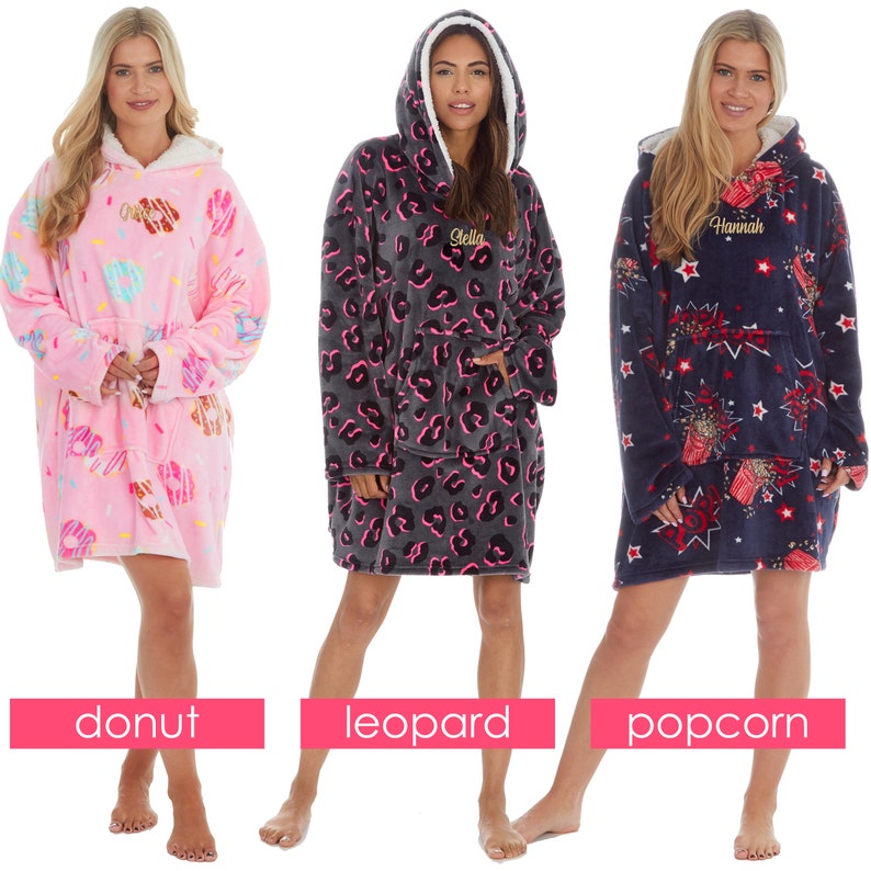 May include: Three oversized hooded blankets with different patterns. The first blanket is pink with a donut pattern. The second blanket is grey with a leopard print. The third blanket is navy blue with a popcorn pattern. Each blanket has a pocket on the front and a hood.