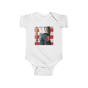 May include: A white short-sleeve baby bodysuit featuring a graphic print of the Born in the U.S.A. album cover. The graphic displays a person wearing a white t-shirt and blue jeans with a red cap in the back pocket against a red and white striped background.