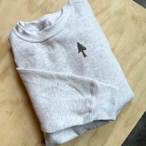 May include: A gray sweatshirt with a green embroidered pine tree on the front.