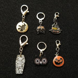 May include: Six Halloween-themed charms with silver and gold metal clasps. The charms include a black cat, a cauldron, a witch's hat, a coffin, an owl, and a jack-o'-lantern.