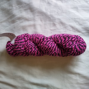 May include: A skein of black and hot pink yarn. The yarn is twisted into a loose coil.