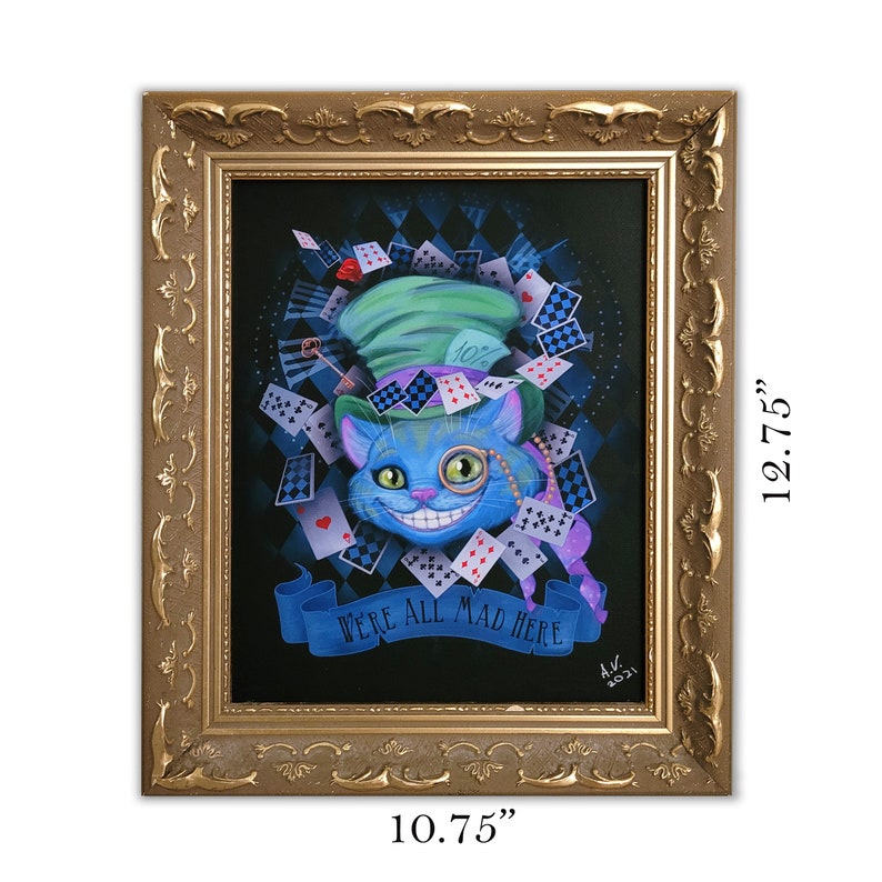 Op de afbeelding: Een ingelijst schilderij van de Cheshire Cat uit Alice in Wonderland. De kat is blauw met een groene hoed en een ondeugende grijns. De achtergrond is zwart met een schaakbordpatroon en speelkaarten. De tekst "We're all mad here" staat op een banner onder de kat. De lijst is goudkleurig met sierlijke details. Het schilderij is 10,75 inch breed en 12,75 inch hoog.