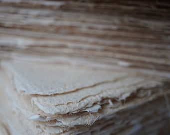 May include: A stack of handmade paper sheets, with a rough, textured surface and a natural off-white color. The paper is made from recycled materials and is perfect for crafting, journaling, and other creative projects.
