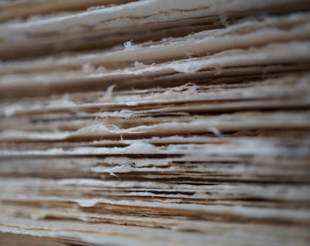 May include: Close-up of a stack of thin, off-white paper sheets, showing the texture and layering of the paper.