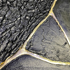 May include: Close-up of a black and gold abstract painting with a textured surface. The gold paint is applied in a thick, uneven line, creating a dramatic contrast against the black background.