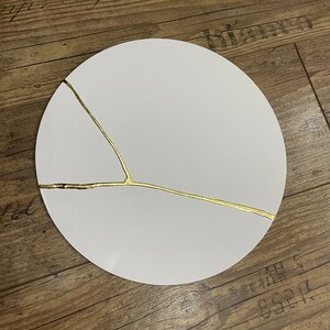 Puede incluir: Un plato redondo blanco con un dise&ntilde;o de craquelado dorado. El plato est&aacute; sobre una superficie de madera.