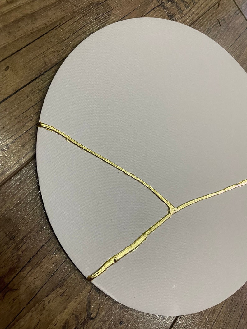 Puede incluir: Un plato redondo decorativo de color blanco roto con un dise&ntilde;o de craquelado dorado.