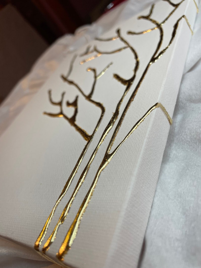 May include: A white canvas with a gold tree design painted on the front. The canvas is wrapped around the edges and has a white background.