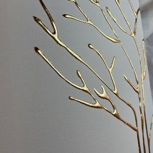 May include: A white canvas with a gold leaf tree design. The tree branches are thin and delicate, creating a minimalist and elegant look.