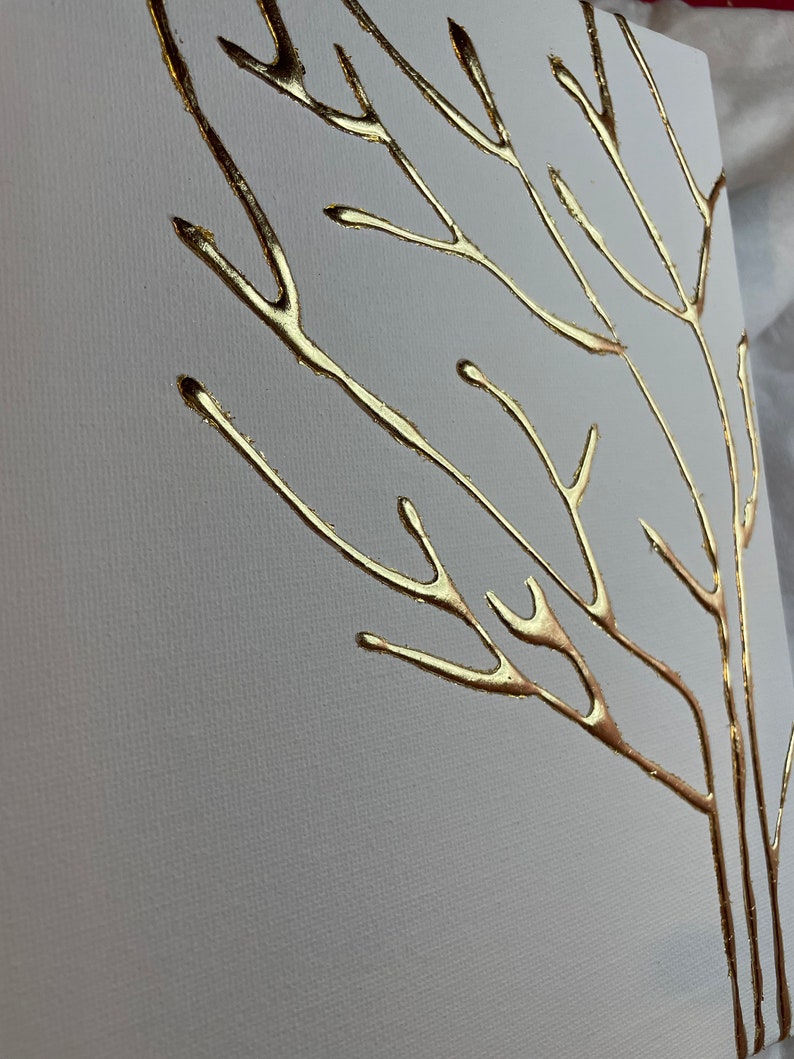 May include: A white canvas with a gold leaf tree design. The tree branches are thin and delicate, creating a minimalist and elegant look.