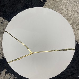 Puede incluir: Una mesa redonda blanca con un dise&ntilde;o de grieta dorada.