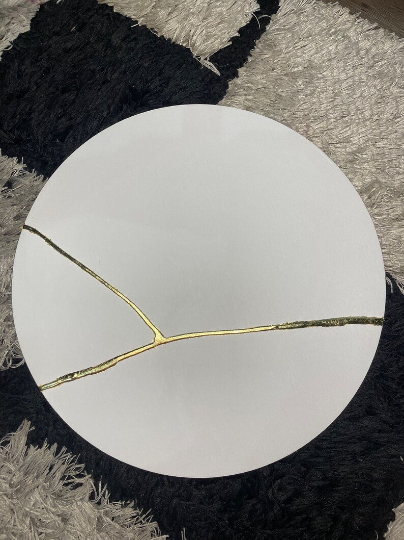 Puede incluir: Una mesa redonda blanca con un dise&ntilde;o de grieta dorada.