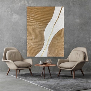 May include: Abstract painting with brown and white textured shapes and a gold line. The painting is hanging on a gray wall above a coffee table with two chairs.
