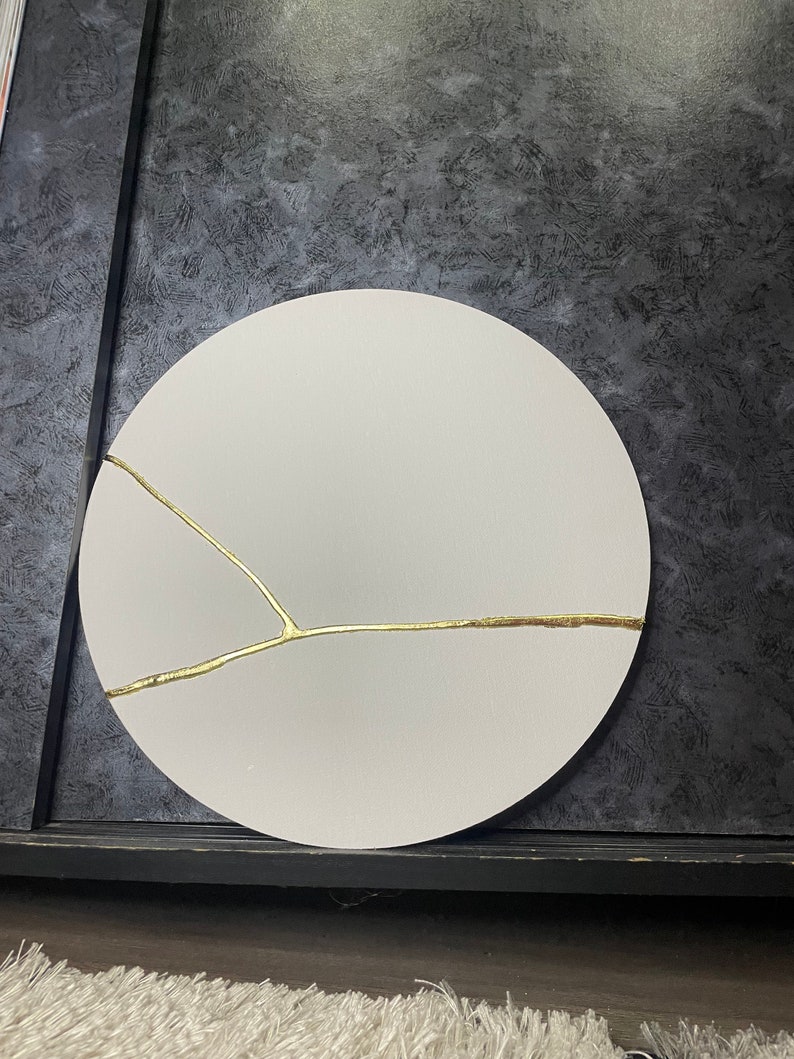 Puede incluir: Un lienzo circular blanco con un dise&ntilde;o de grietas doradas. El lienzo est&aacute; sobre un fondo gris oscuro.