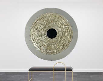 May include: A large circular wall art piece with a textured gold surface and a black circle in the center. The art is hanging on a white wall above a black leather bench with a gold metal frame.