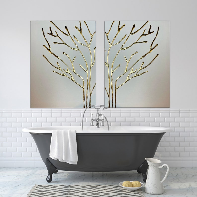 May include: A black freestanding bathtub with a white towel draped over the side. Two gold framed paintings of stylized trees hang above the tub. The paintings are on a white tiled wall.