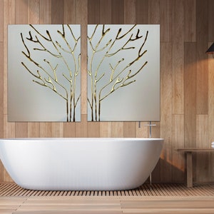 May include: A white bathtub sits in a bathroom with wood paneling on the walls. Two framed pieces of art with gold leaf tree branches hang above the tub. A wooden shelf with a towel and a bottle of soap sits on the right side of the image.