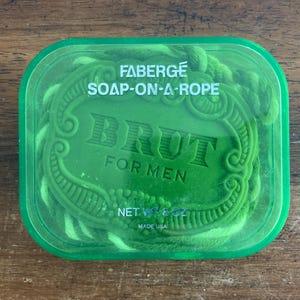 May include: Green Faberge Brut Soap-on-a-Rope in a clear plastic container. The soap is green and has the words "BRUT FOR MEN" embossed on it. The net weight is 8 oz. Made in the USA.
