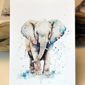 Pu&ograve; includere: Dipinto ad acquerello di un cucciolo di elefante in piedi su uno sfondo di schizzi blu e bianco. L'elefante &egrave; di colore marrone chiaro con una proboscide e orecchie di colore grigio chiaro.